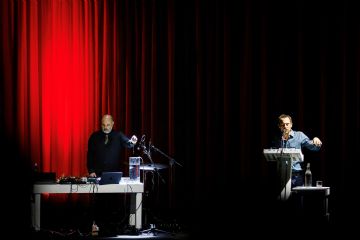 Elio Germano su di un palcoscenico privo di scenografie con davanti un leggio interpreta un testo