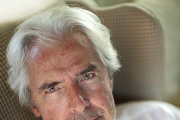 Tullio Solenghi in camicia bianca su sfondo neutro e con sguardo verso l'obiettivo con espressione intensa