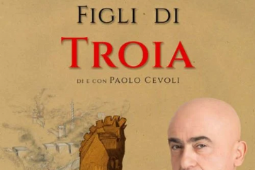 Paolo Cevoli con armatura punta il dito verso lo spettatore, sullo sfondo un cavallo di Troia e la città cinta da mura